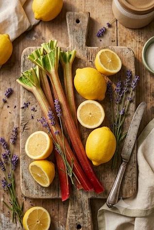 A flatlay of rhubarb, lemons and lavender sprigs on a wooden board