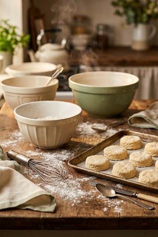 A rustic kitchen counter mid-bake with mixing bowls, a whisk and a tray of scones